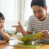 Anak kecil berwajah bosan ketika ibu bapa menunjukkan buku yang tidak menarik minatnya, melambangkan kesilapan memilih bahan bacaan.