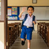 Kanak-kanak Melayu berpakaian seragam sekolah sambil tersenyum lebar dan melambai tangan, menunjukkan semangat dan keyakinan untuk