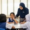 Anak Asia berseragam sekolah belajar dalam kumpulan kecil bersama guru dengan suasana tenang dan mesra.
