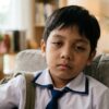 Close-up wajah murid Asia berseragam sekolah yang kelihatan letih dan kurang bertenaga selepas pulang dari sekolah.