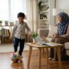 Anak Asia bermain bola di ruang rumah manakala buku terletak di atas meja, ibu bapa memerhati dengan tenang.