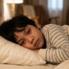 Anak Asia masih terjaga di atas katil walaupun nampak mengantuk, menunjukkan badan belum cukup bersedia untuk tidur.